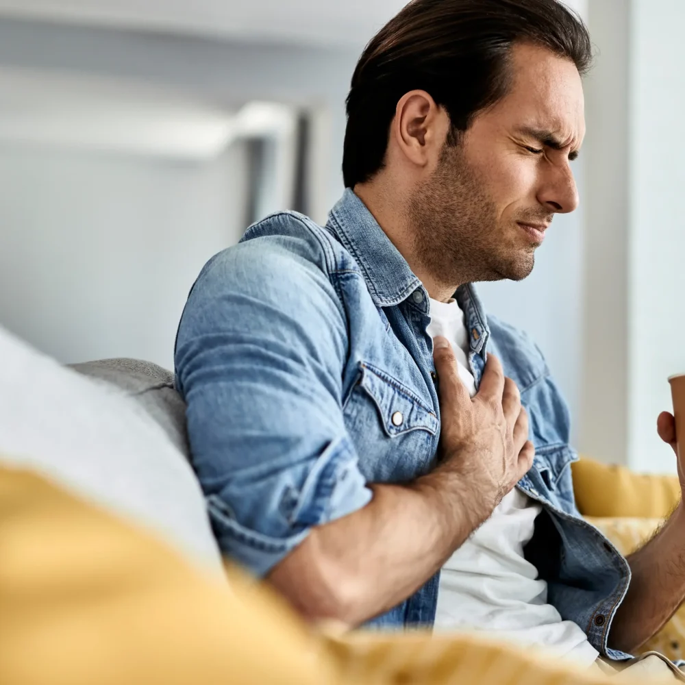 young-man-feeling-sick-holding-his-chest-pain-while-drinking-tea-living-room